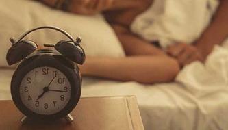 A woman lies in bed looking at the alarm clock.